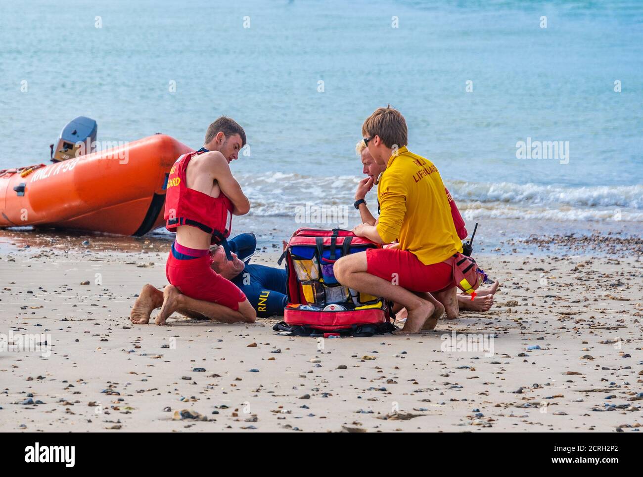 Rettungsschwimmer gehen durch medizinische Rettungsschwimmer Ausbildung an einem Strand, zeigt jemand spielen die Rolle eines verletzten Patienten am Meer, in Großbritannien. Stockfoto