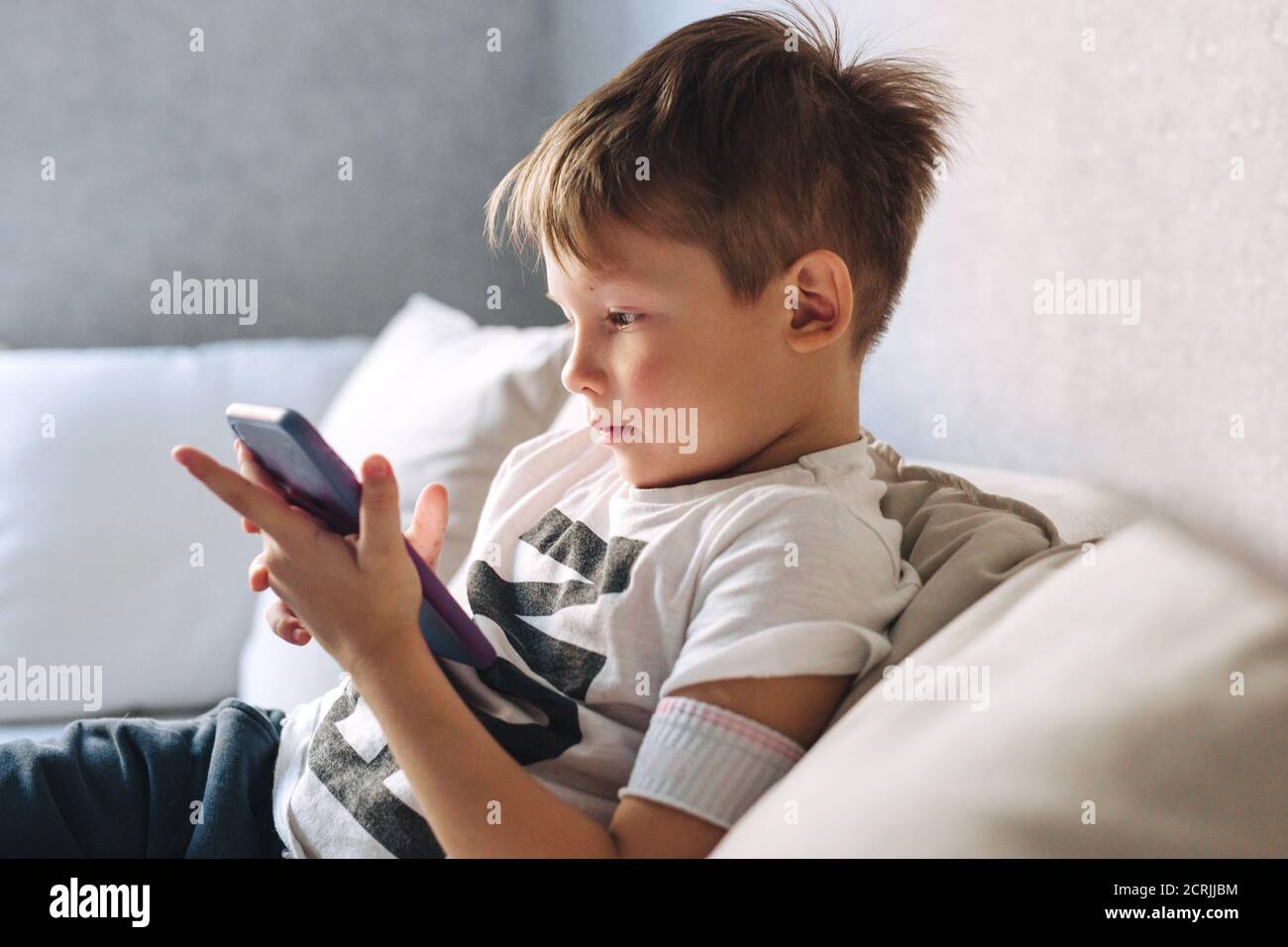 Kleiner Junge sitzen auf dem Sofa und telefonieren zu Hause Stockfoto