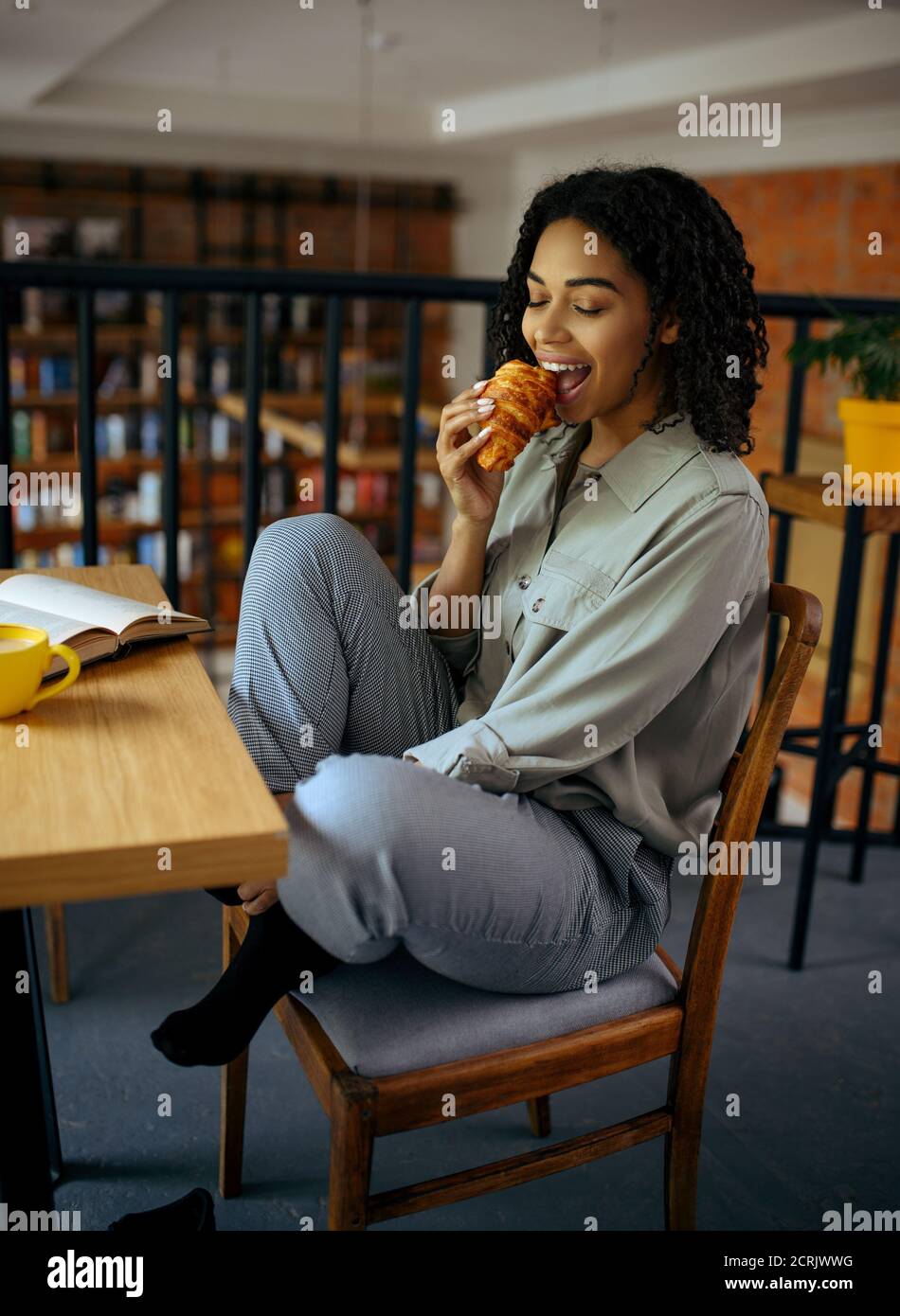 Nette Studentin isst Croissants im Café Stockfoto