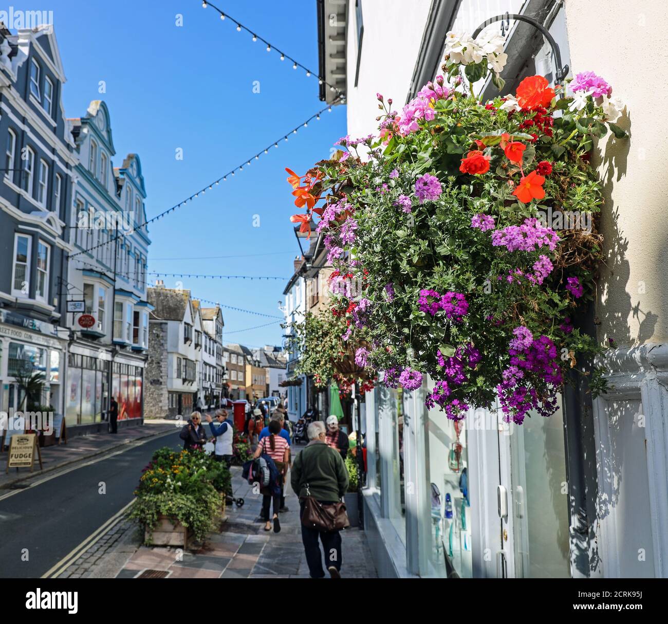 Ein farbenfroher Blumenkorb verleiht der Southside Street in Plymouth Farbe. Das historische Barbican bietet eine schrullige Mischung aus kleinen Geschäften, öffentlichen Häusern und Restaurants Stockfoto