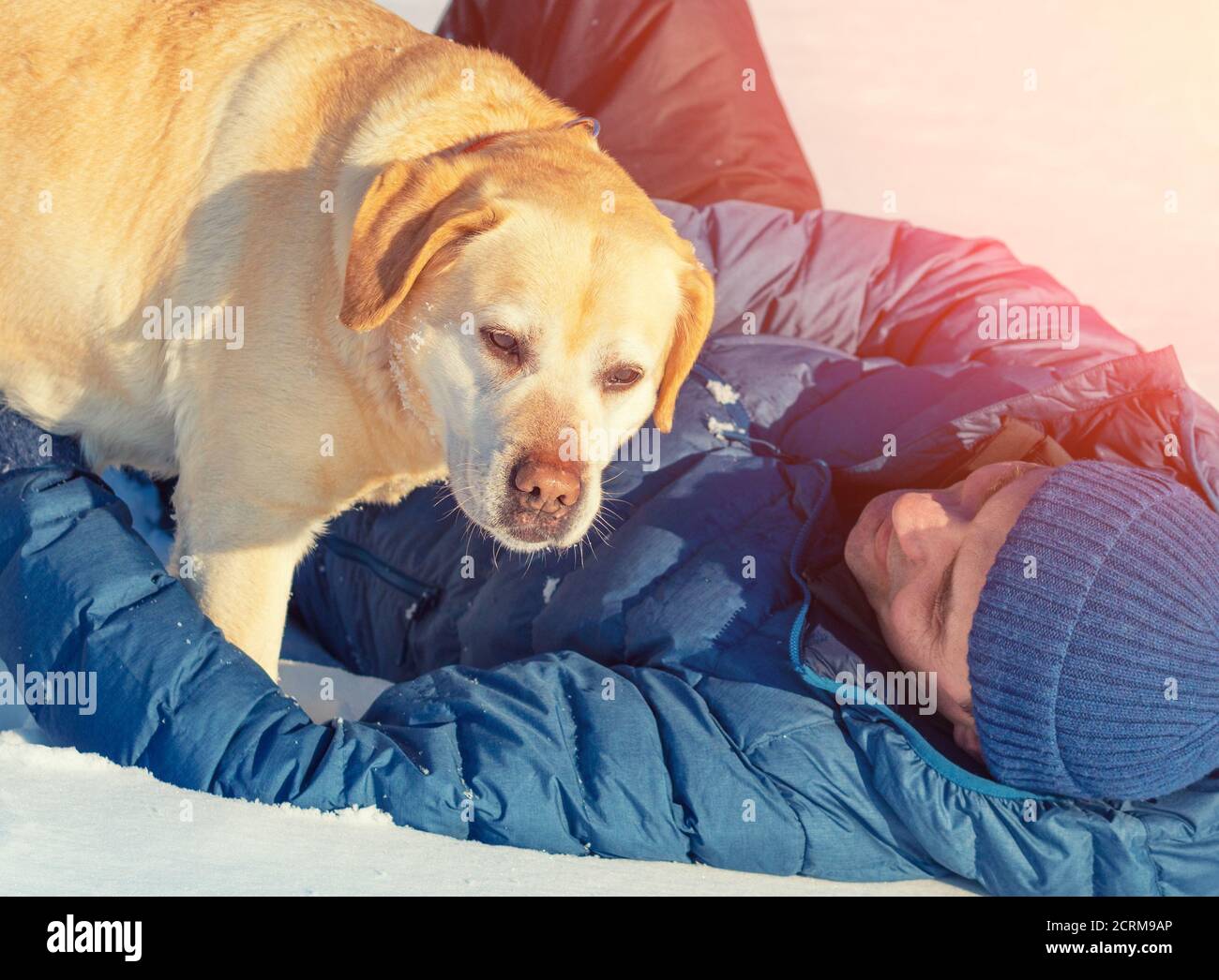 Ein glücklicher lächelnder Mann mit einem Labrador Retriever Hund liegt Im Schnee im Winter Stockfoto