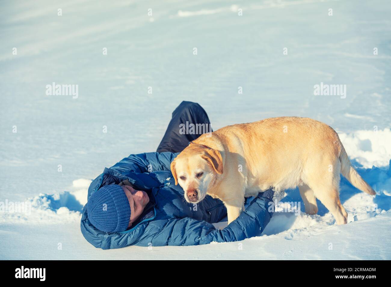 Ein glücklicher lächelnder Mann mit einem Labrador Retriever Hund liegt Im Schnee im Winter Stockfoto