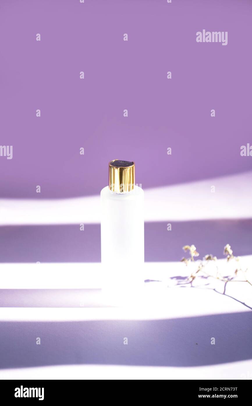 Matte Kosmetikflasche mit goldenem Deckel auf violettem Hintergrund Stockfoto