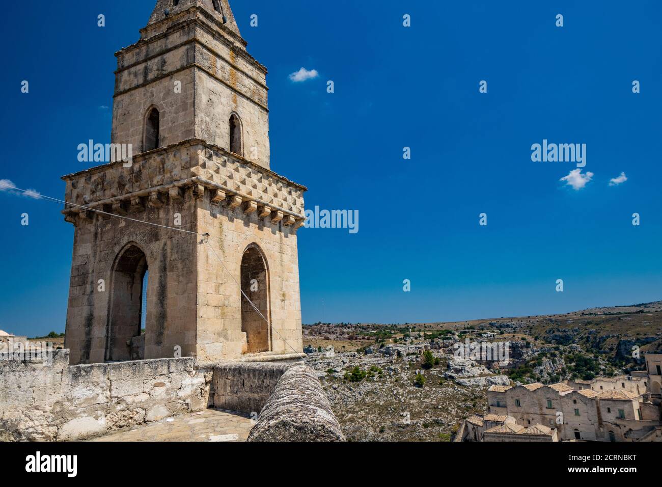 Matera, Basilicata, Italien - der Glockenturm der Höhlenkirche von San Pietro Barisano, mit dem Murgia Maternana Park im Hintergrund. Stockfoto