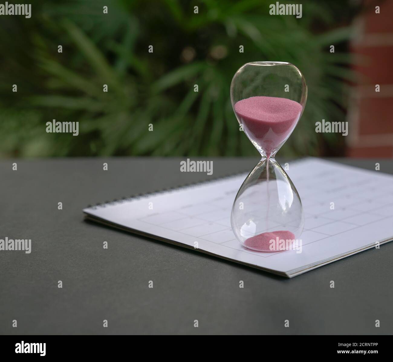 Stunde Glas mit Sand fließt, sitzen auf Kalender. Zeitvergehen, Countdown oder Deadlines Konzept. Stockfoto
