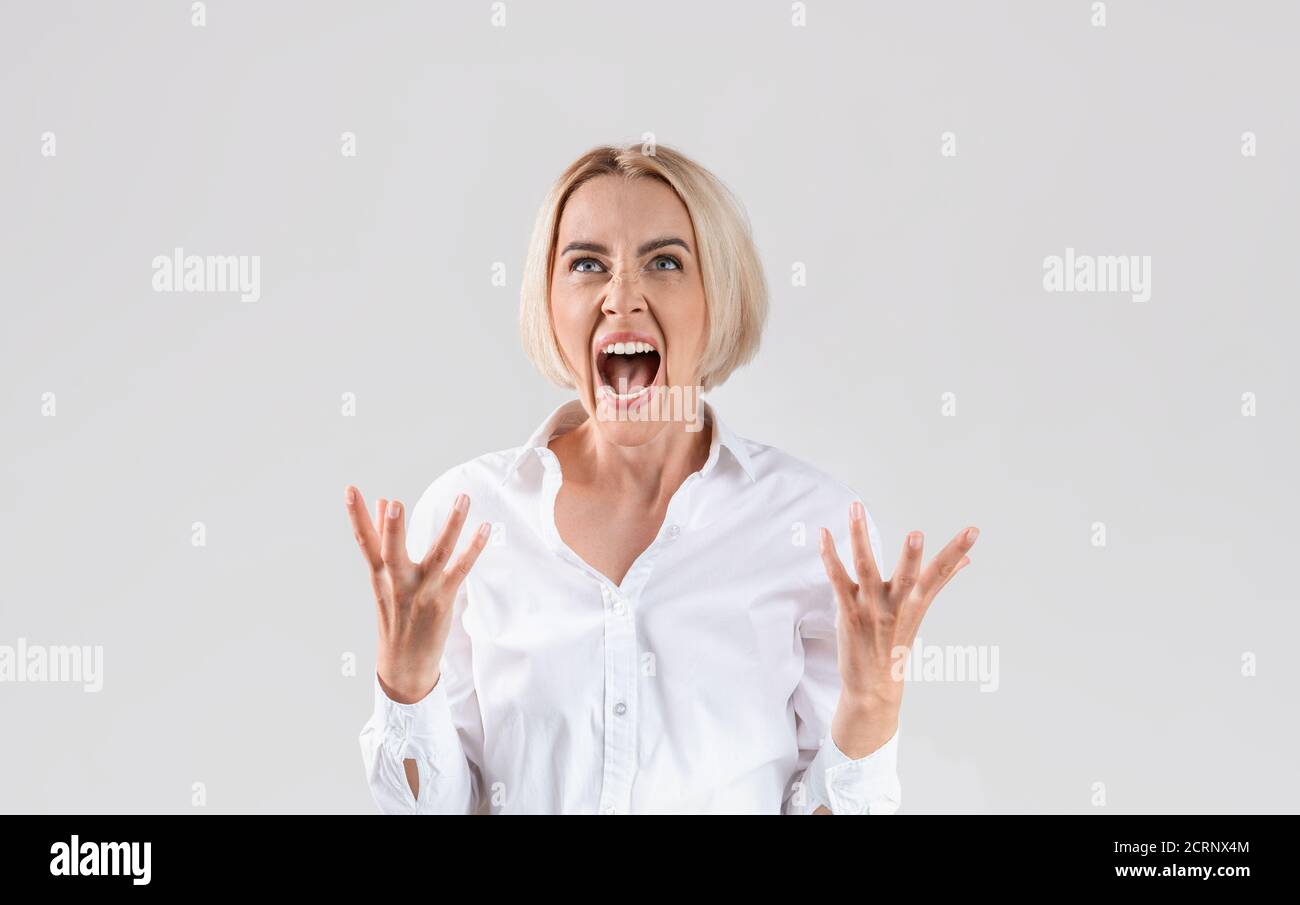 Schöne blonde Geschäftsfrau im Büro tragen schreien in Wut auf Heller Studiohintergrund Stockfoto