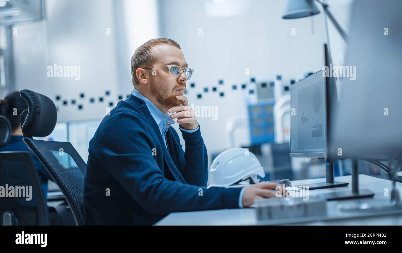 Shot von Male Industrial Engineer Probleme lösen, Arbeiten an einem Personal Computer, Er arbeitet im Büro in der modernen Fabrik mit High-Tech-Maschinen. Stockfoto