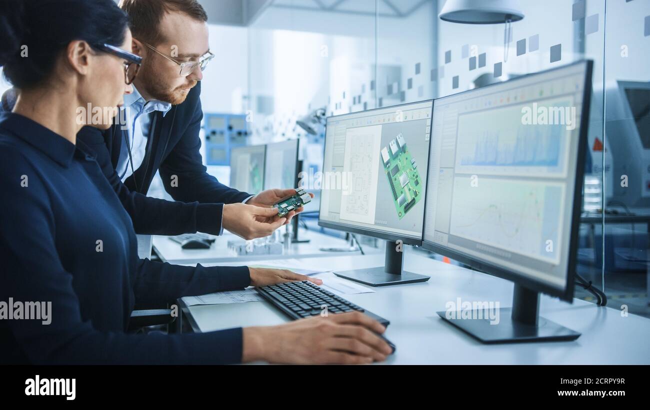 Moderne Elektronikfabrik: Männlicher Vorgesetzter spricht mit einer weiblichen Elektroingenieurin, die auf Computer mit CAD-Software arbeitet. Entwicklung von Leiterplatten, Mikrochips Stockfoto