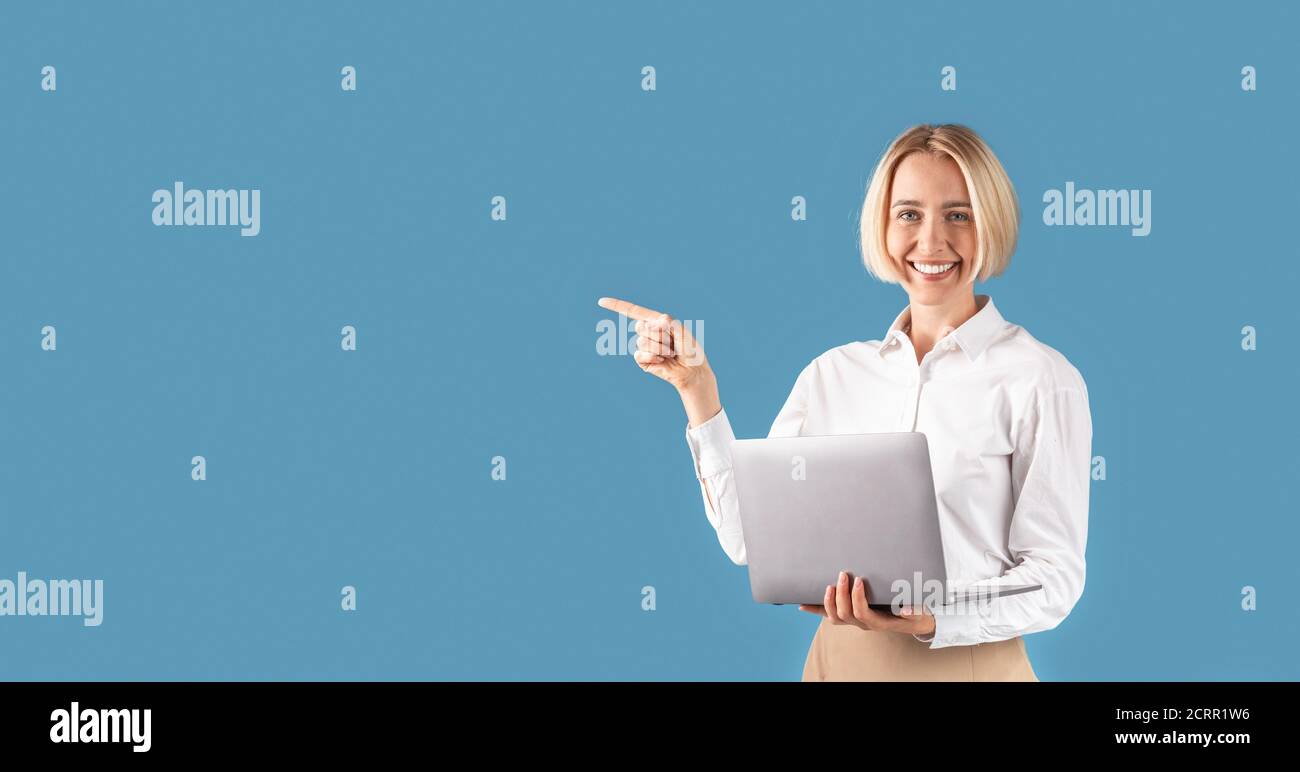 Glückliche Geschäftsfrau mit Laptop-Computer zeigt beiseite auf Platz für Ihren Text, blauen Studio-Hintergrund Stockfoto