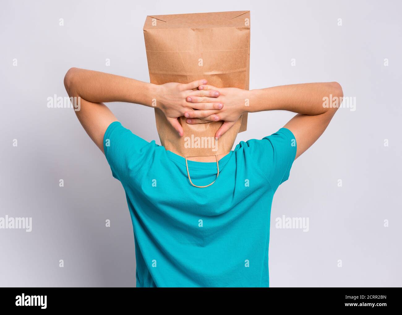 Porträt des Teenagers - Rückansicht, mit Papiertüte über dem Kopf, die Ruhe nimmt, auf grauem Hintergrund. Zeit zum Entspannen. Kind hält die Hände hinter seinem Kopf mit Stockfoto