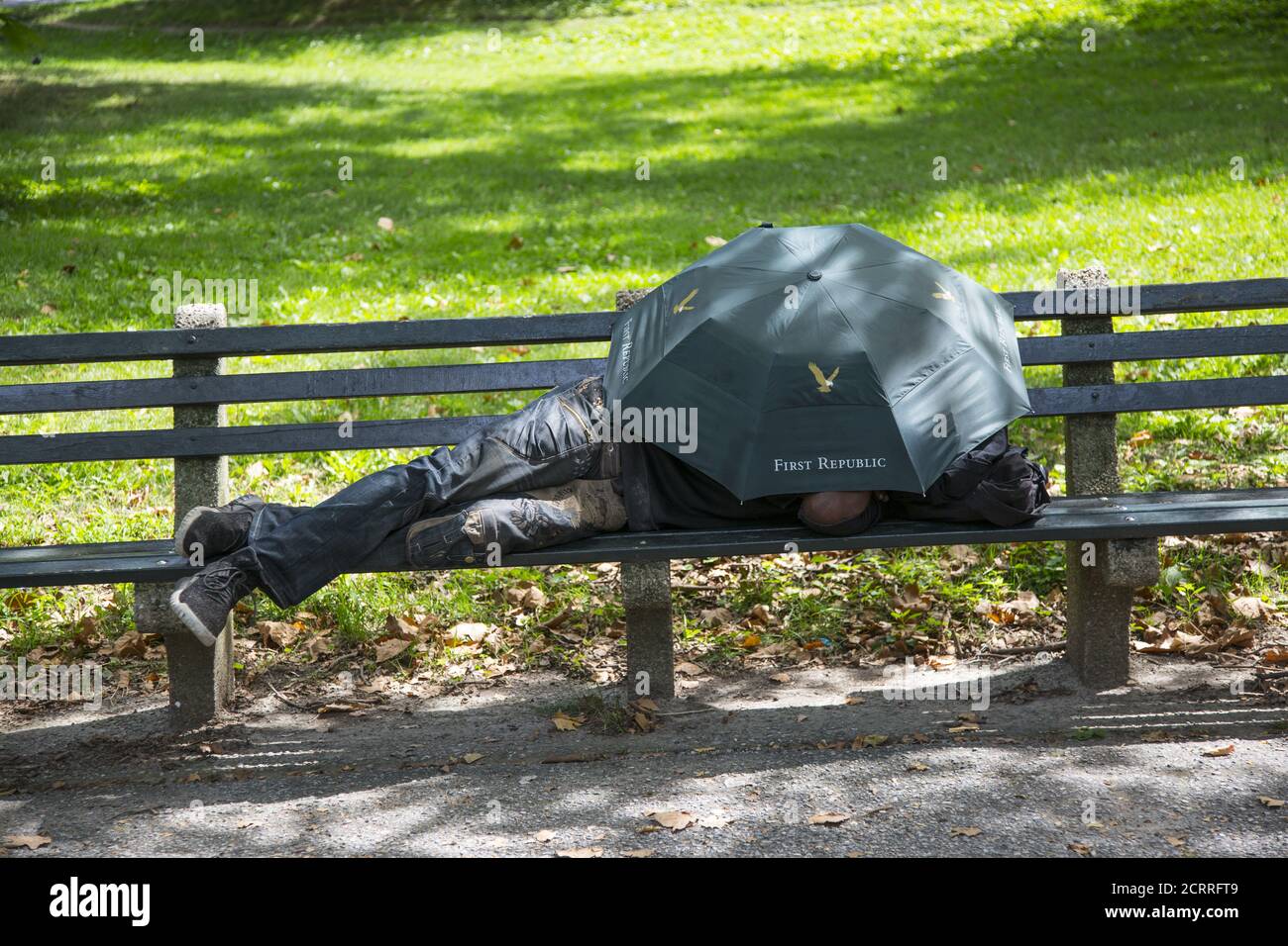 Mann schläft auf einer Bank unter einem Sonnenschirm im Central Park, New York City. Stockfoto
