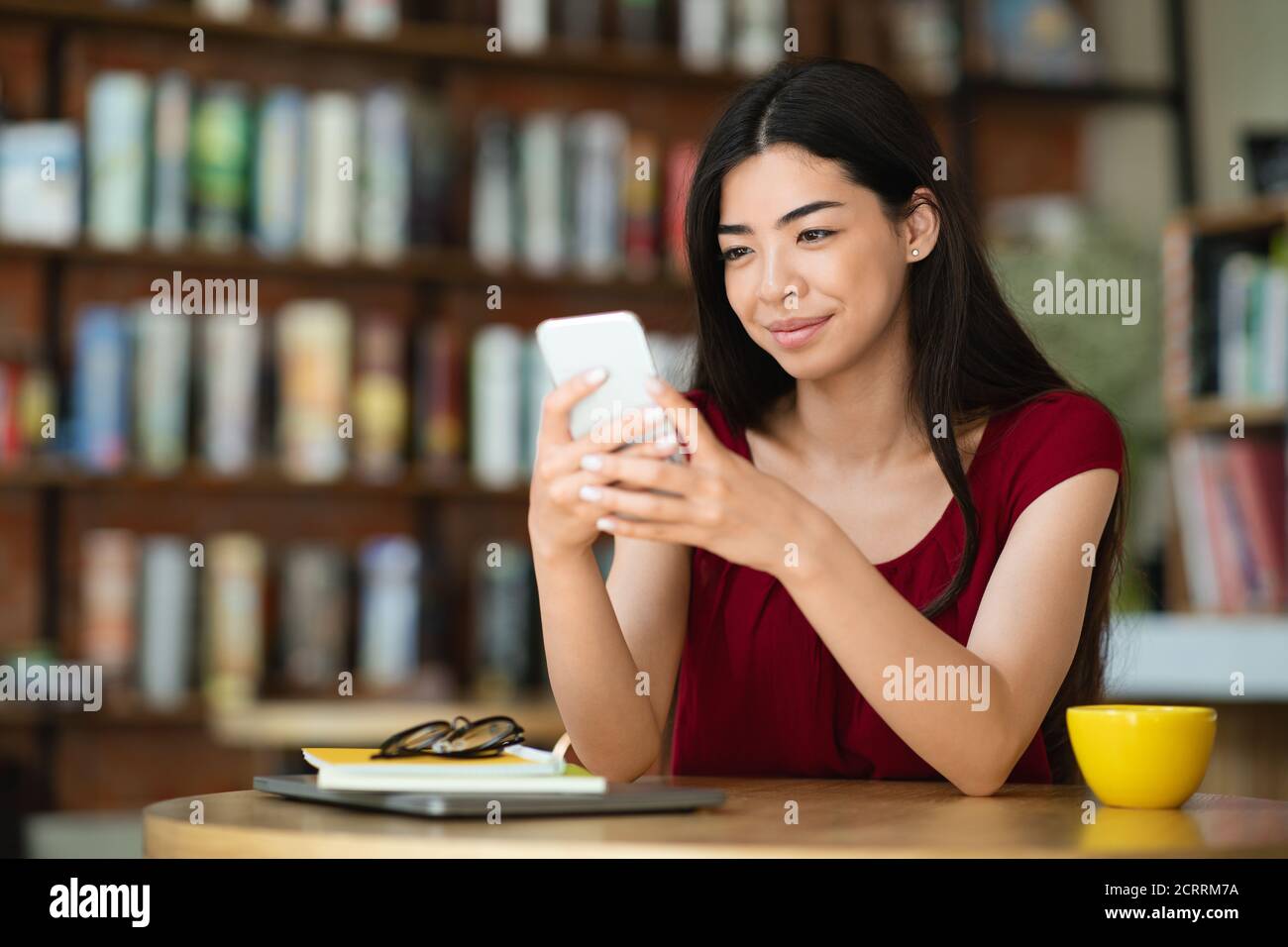 Lächelnde Asiatische Frau Sitzt Im Café Mit Smartphone, Sms Lesen Und Lächeln Stockfoto