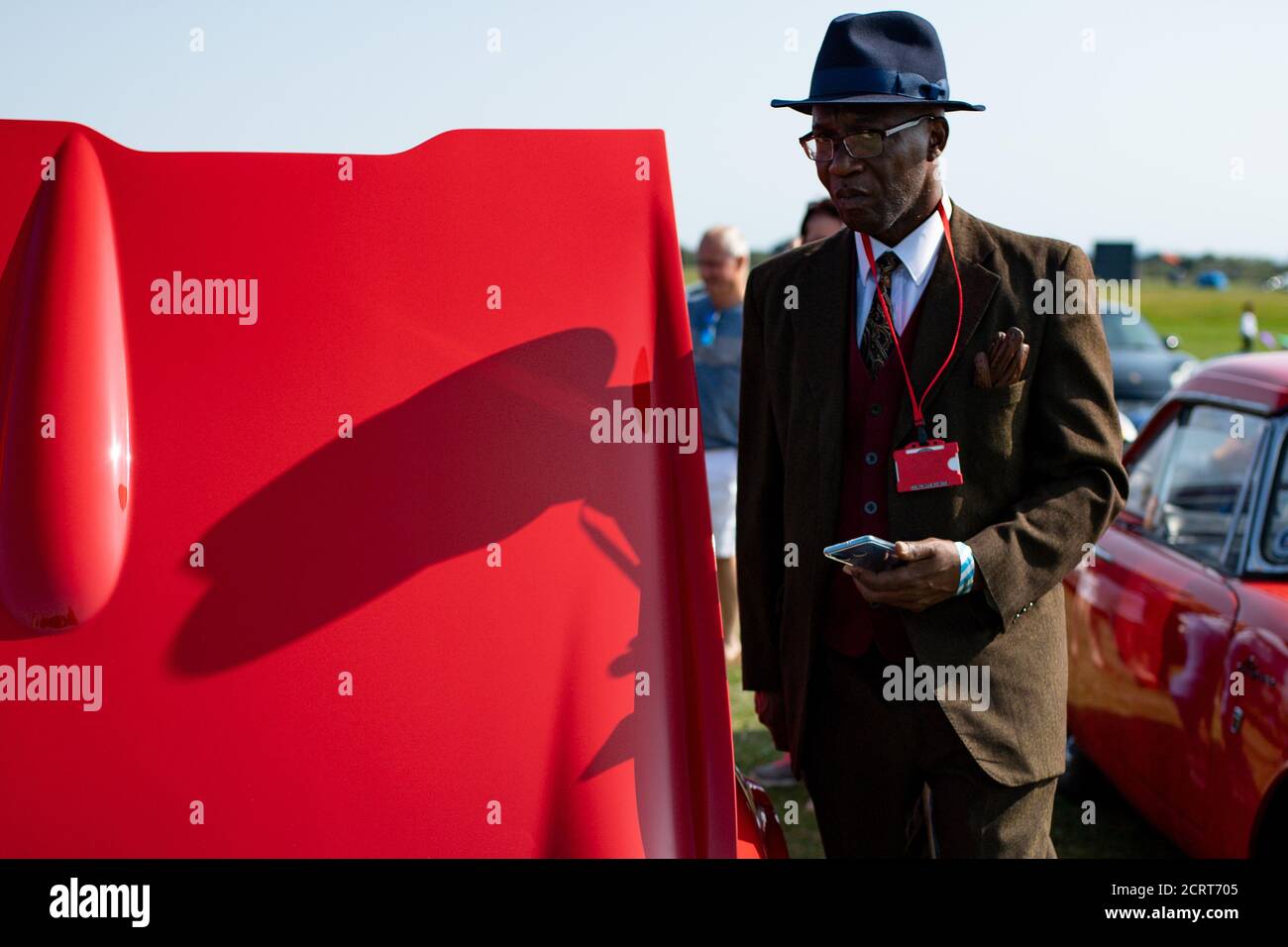 Ein Mitglied des Afro-Caribbean Classic and Sports Car Club steht bei Einem Triumph Herald während der Veranstaltung Classic Car Drive in Weekend im Bicester Heritage. Stockfoto