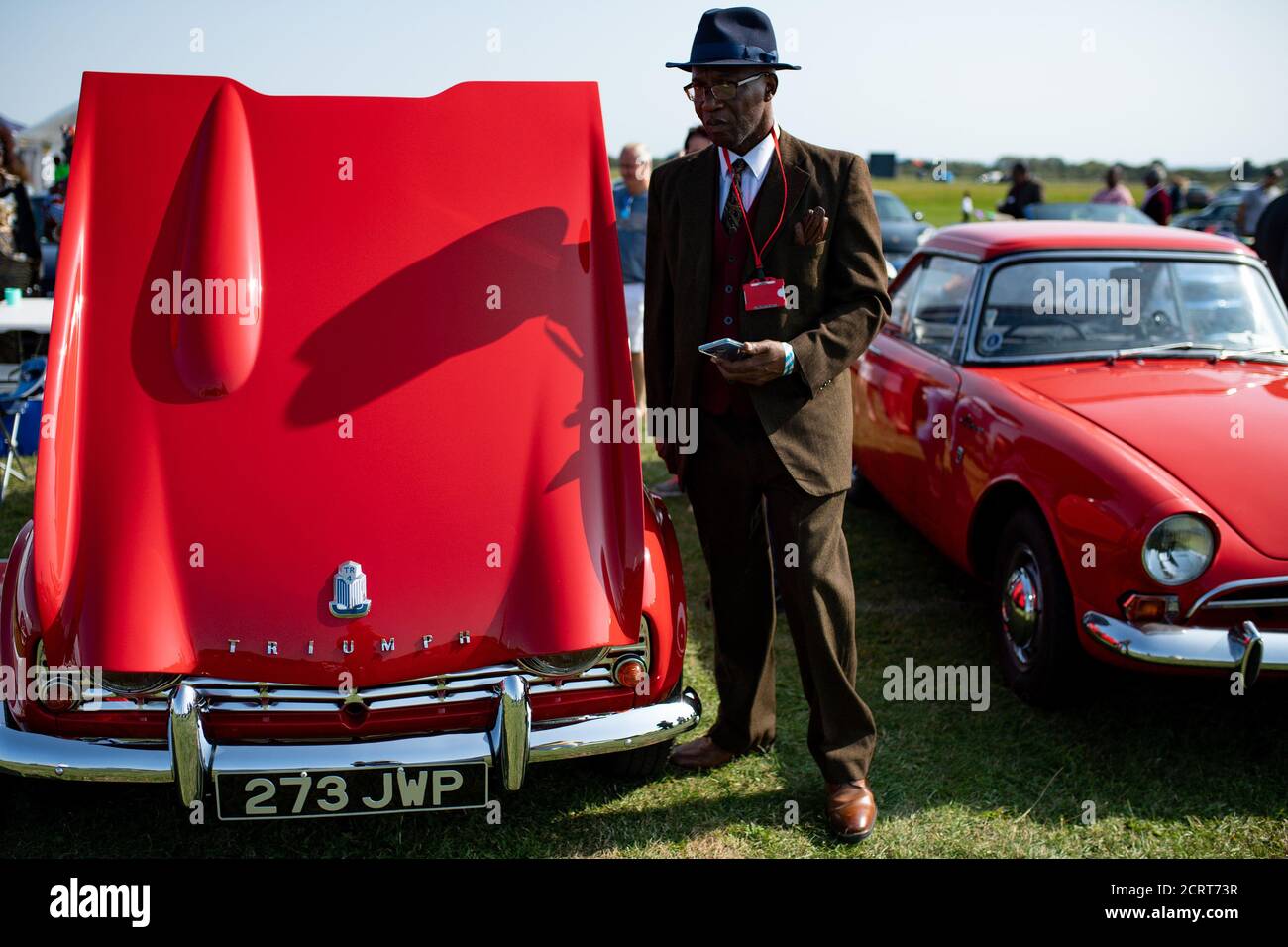Ein Mitglied des Afro-Caribbean Classic and Sports Car Club steht bei Einem Triumph Herald während der Veranstaltung Classic Car Drive in Weekend im Bicester Heritage. Stockfoto