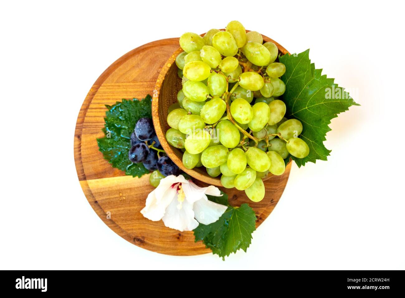 Trauben und Hibiskusblüten auf einem Holzbrett. Weißer Hintergrund. Stockfoto