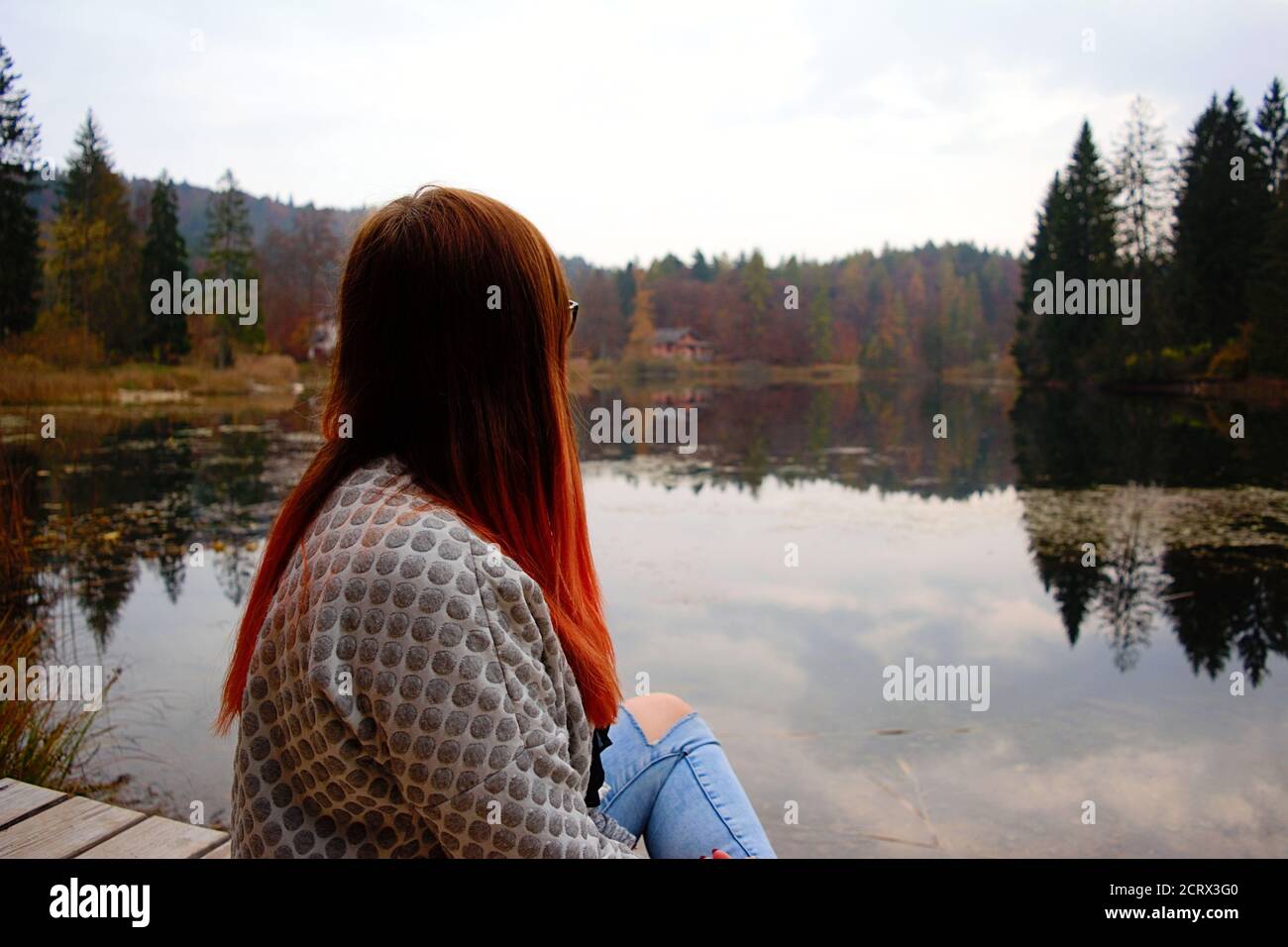 Rote Haare Mädchen in der Nähe von See während der Herbstsaison mit Laub und Wasserspiegelung Stockfoto