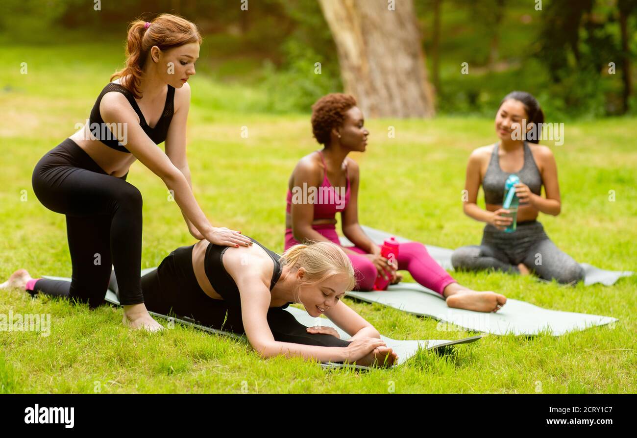 Junge multinationale Damen üben Yoga mit Trainer während der Outdoor-Klasse Im Park Stockfoto