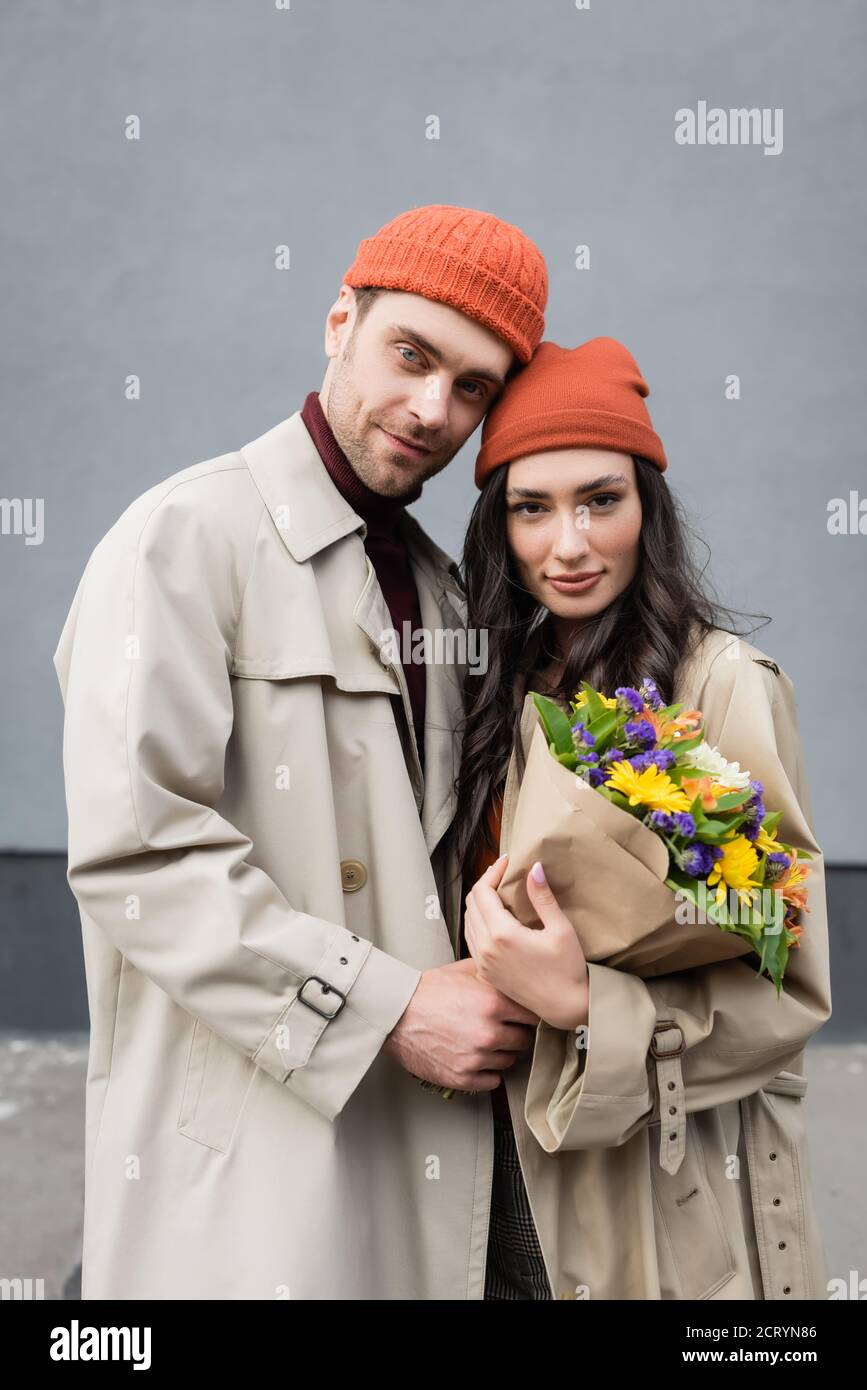 Stilvolles Paar in Trenchcoats und Hüte halten Bouquet von Blumen Stockfoto