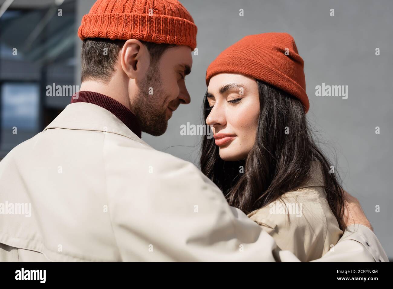 Modisches Paar mit geschlossenen Augen in Trenchcoats und Hüten Stockfoto