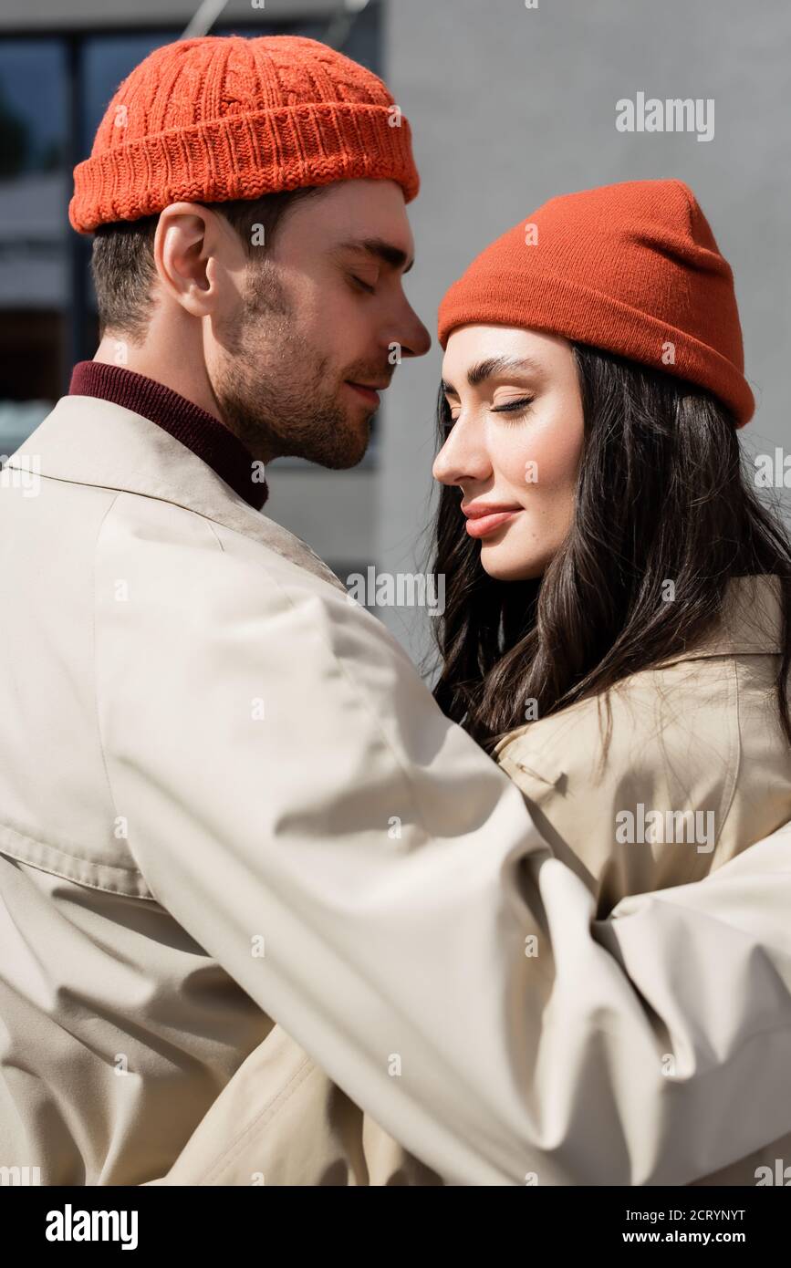 Stilvolles Paar mit geschlossenen Augen in Trenchcoats und Hüten Stockfoto
