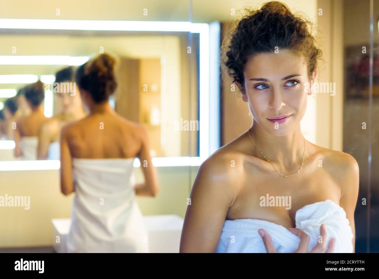 Hübsches Mädchen in einem weißen Handtuch gewickelt bewundern sich in Ein Badezimmerspiegel mit der Reflexion wiederholt mehrmals in Eine Änderung der zurückgehenden Perspektive Stockfoto