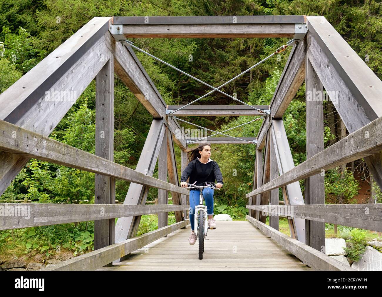 Junges Mädchen, das mit dem Fahrrad über einen Wald und Eisen reitet Fußgänger- und Fahrradbrücke im Grünen in einem Konzept Eines gesunden aktiven Lebensstils Stockfoto