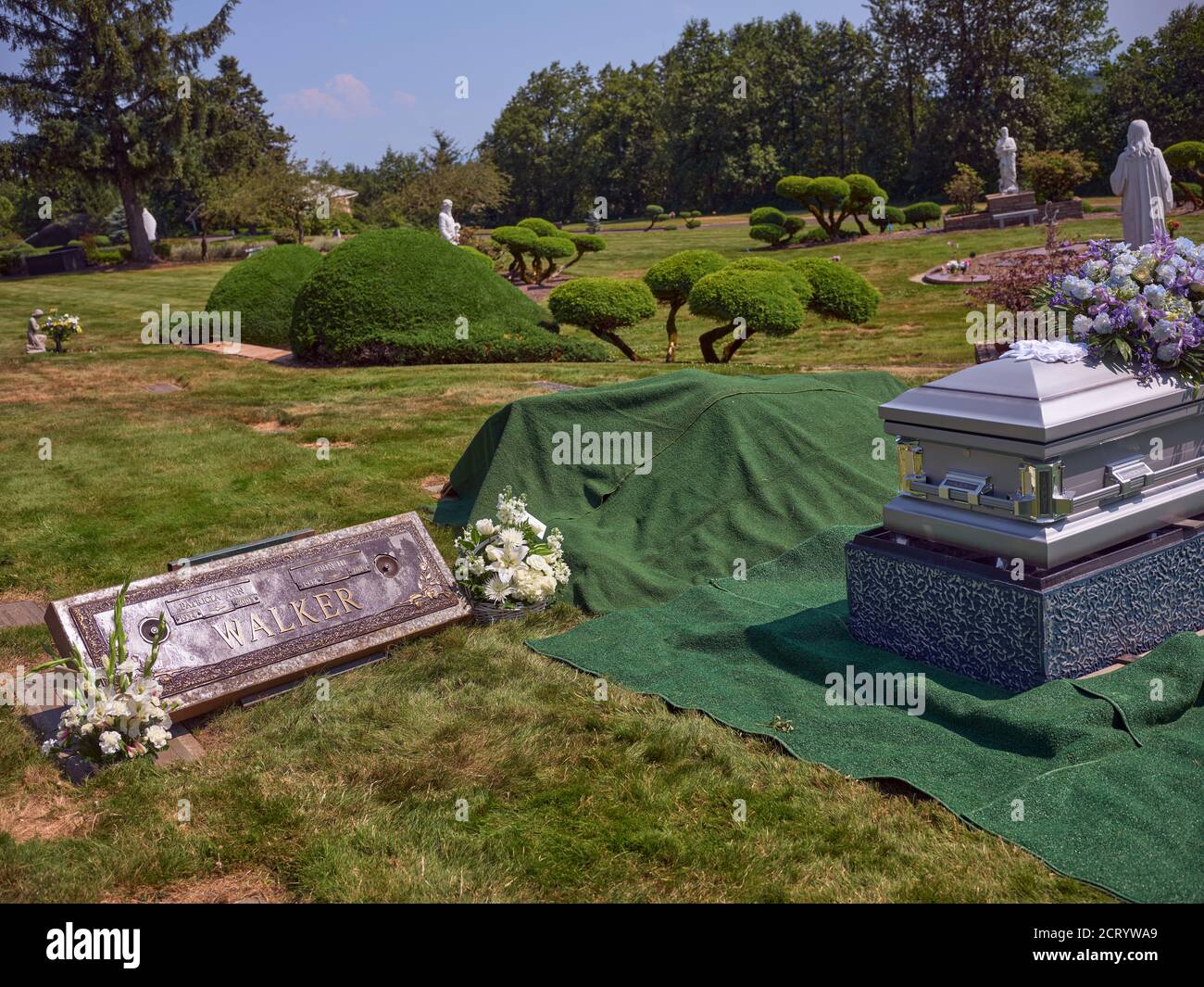 Eine Schatulle mit Blumen sitzt neben einem Grab bereit für die Beerdigung. Stockfoto