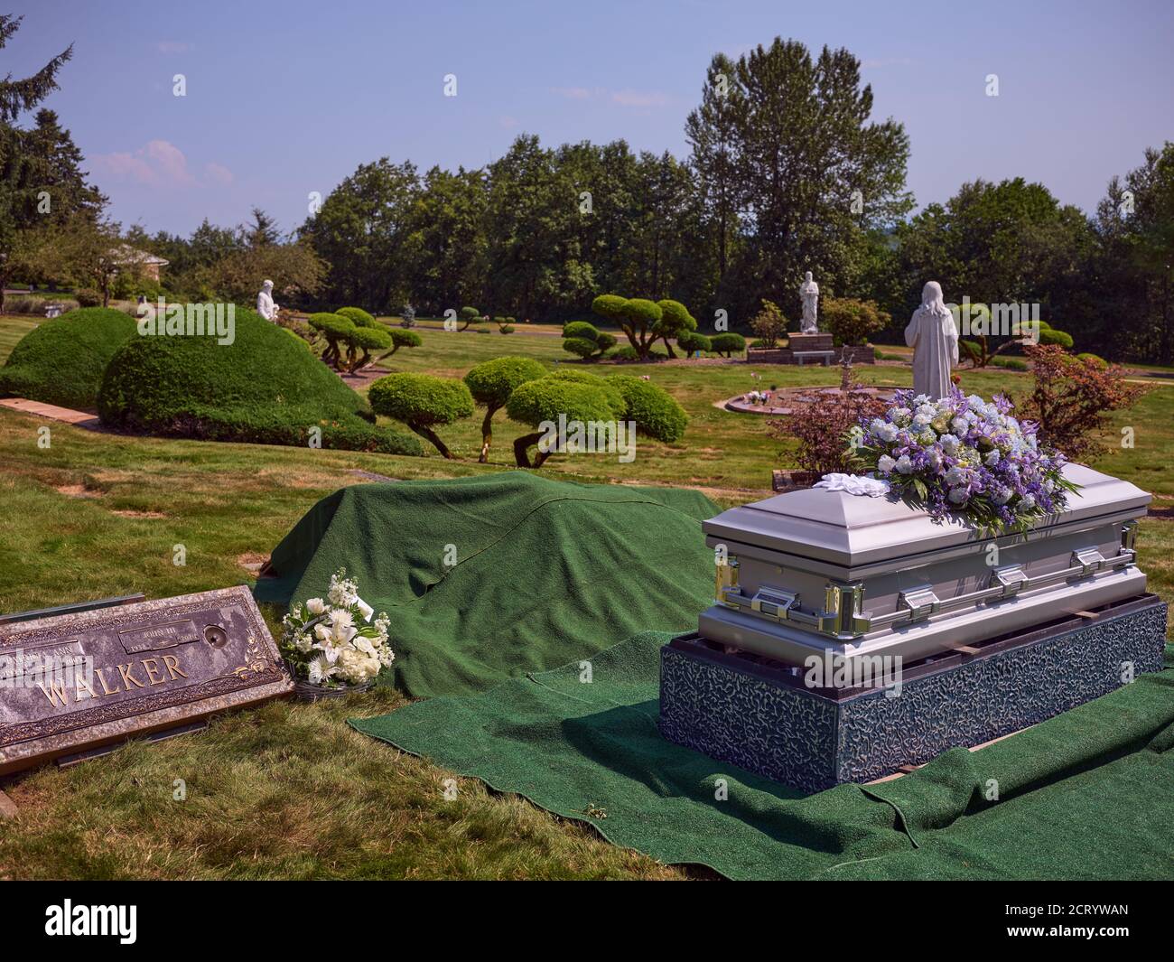 Eine Schatulle mit Blumen sitzt neben einem Grab bereit für die Beerdigung. Stockfoto