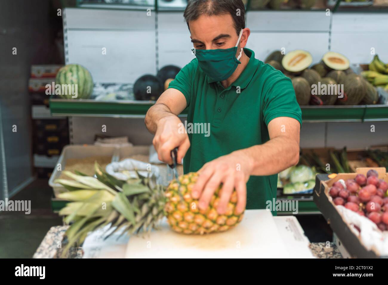 Ein Mann, der in seinem eigenen Obstladen eine Ananas schneidet. Store-Konzept Stockfoto