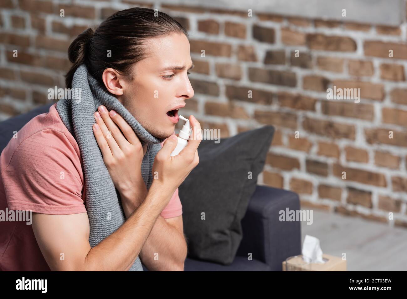 Kranke junge Mann in warmen Schal mit Kehlspray während Berühren des Halses Stockfoto