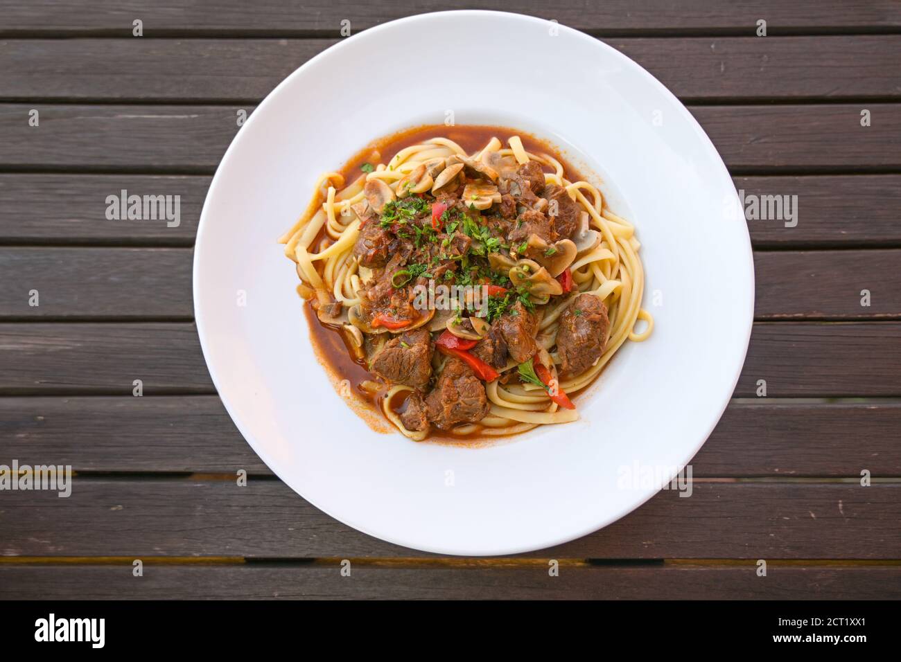 Rindfleisch-Ragout mit roten Paprika und Champignons mit Petersilie garnieren auf hausgemachten Nudeln in einem weißen Teller auf einem rustikalen dunklen Holztisch, Blick in den hohen Winkel Stockfoto