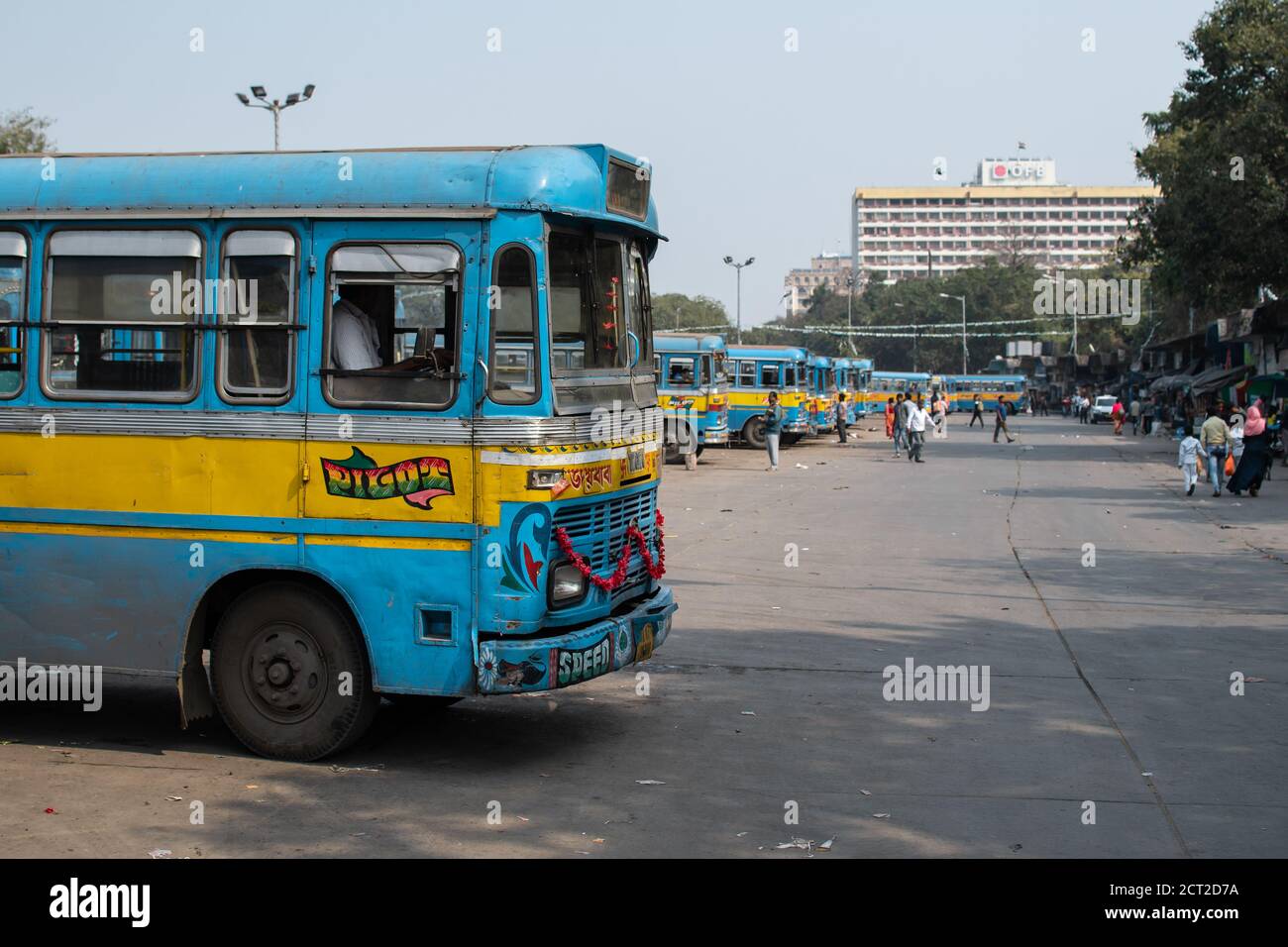 Kolkata, Indien - 1. Februar 2020: Mehrere unbekannte Menschen gehen an traditionellen türkis-gelben öffentlichen Bussen vorbei, die an einer Bushaltestelle parken Stockfoto