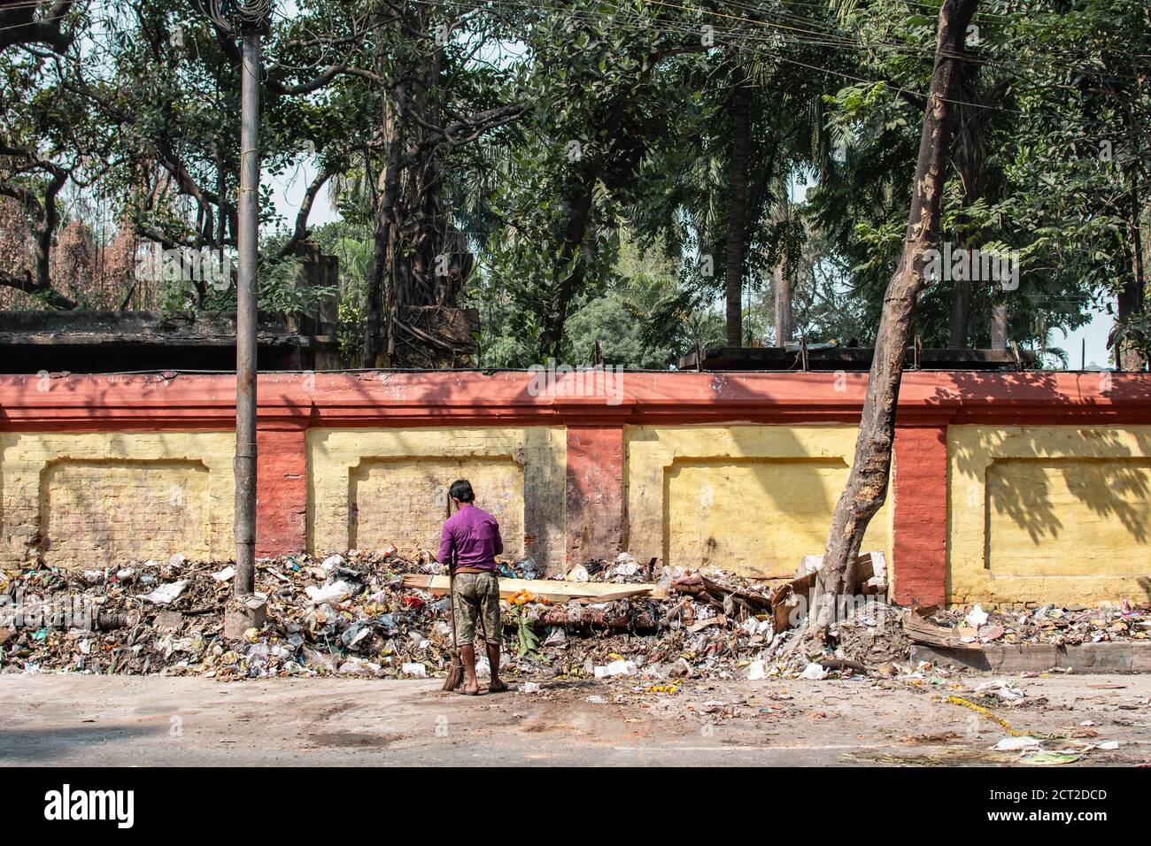 Kolkata, Indien - 1. Februar 2020: Ein nicht identifizierter Mann in purpurfarbenem Hemd steht mit einem Besen vor einem großen Haufen Plastikmüll Stockfoto