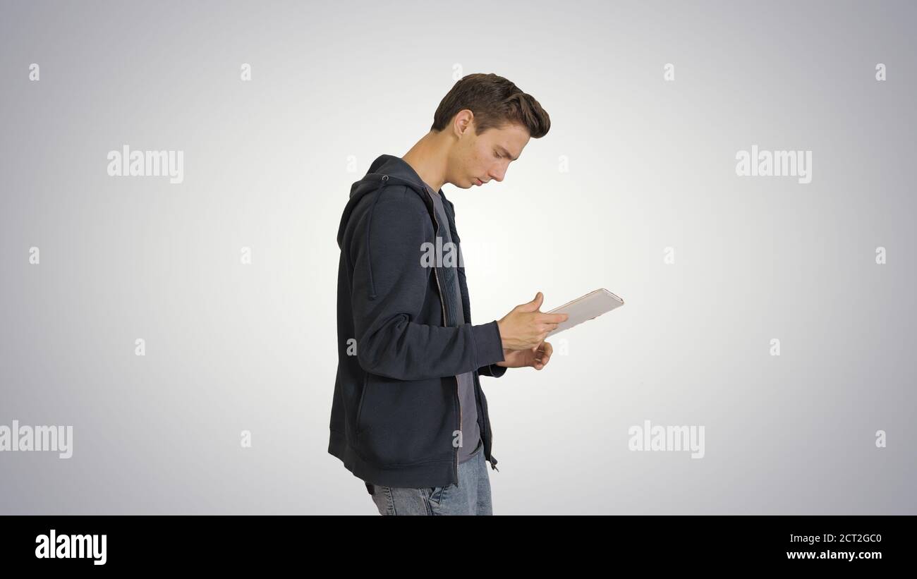 Junger Mann mit digitalen Tablet beim Gehen auf Gradient Backgro Stockfoto