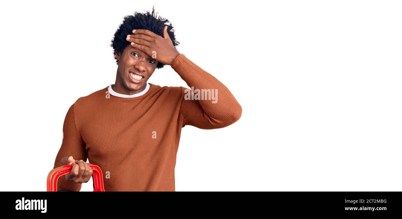 Schöner afroamerikanischer Mann mit afro Haar hält Supermarkt Warenkorb gestresst und frustriert mit Hand auf Kopf, überrascht und wütend Gesicht Stockfoto