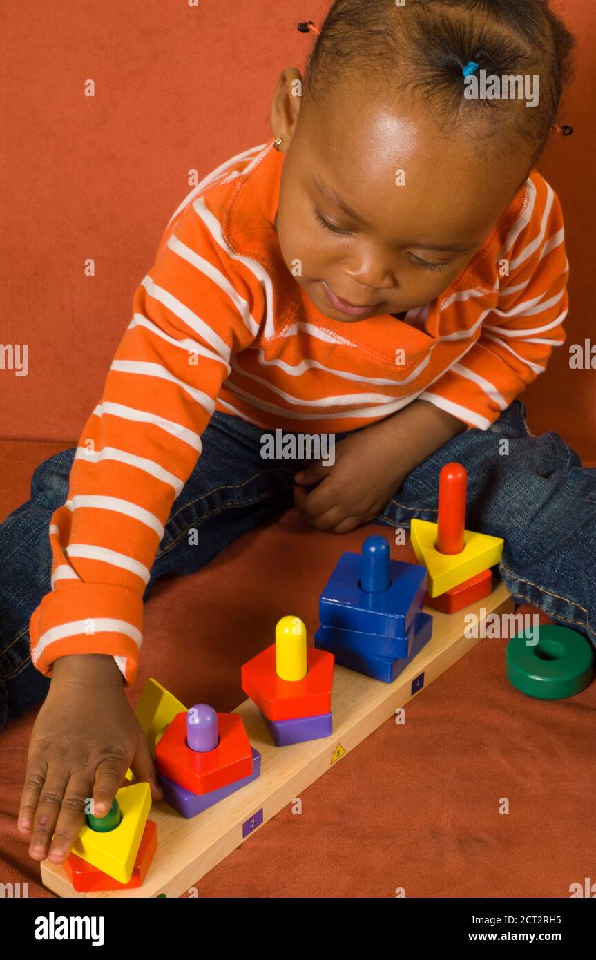 20 Monate alt Kleinkind Baby Mädchen spielen mit bunten Spielzeug Hölzerne geometrische Form Sortierer vertikal Stockfoto