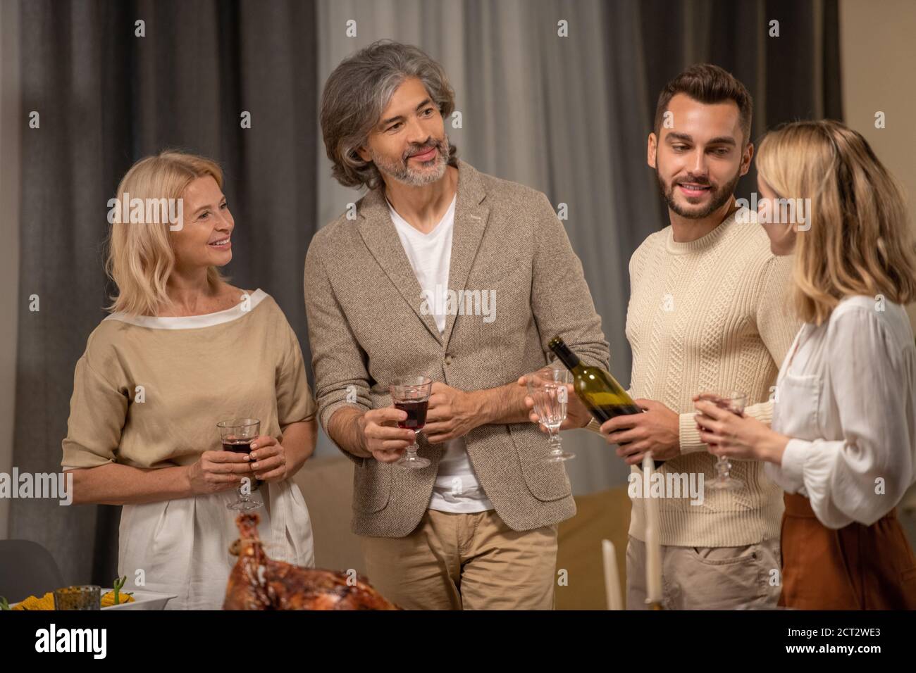 Glückliches reifes Paar mit Gläsern Wein und jungen Mann Blick auf blonde Frau Stockfoto