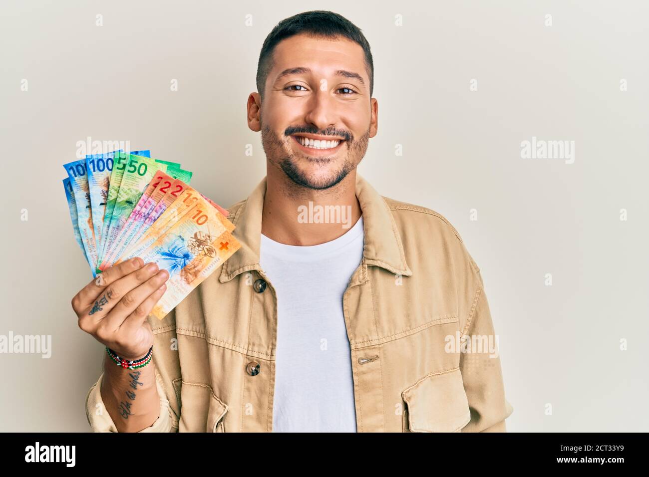 Schöner Mann mit Tätowierungen, die Schweizer FrankenBanknoten halten