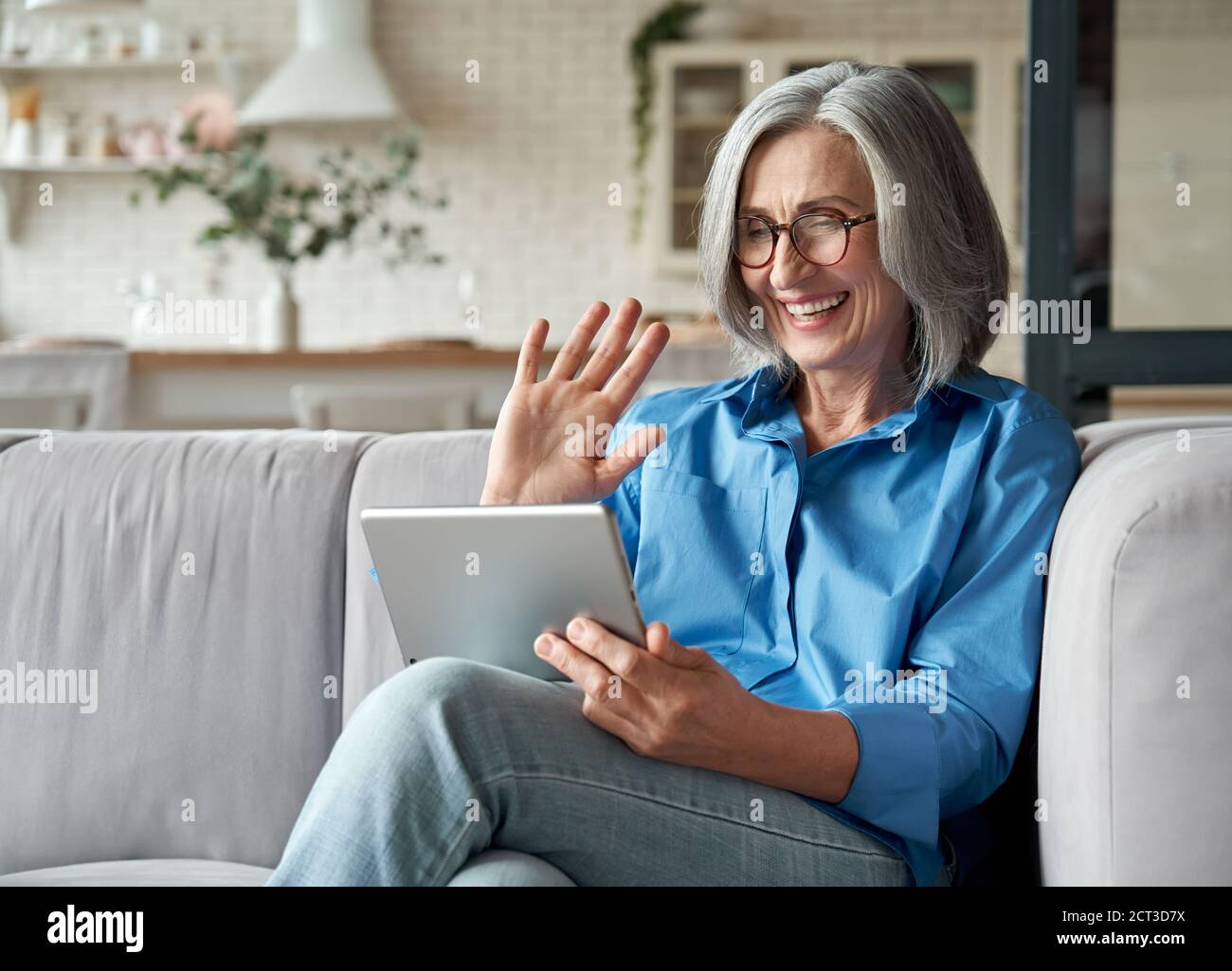 Glückliche 60er Jahre reife Frau winken Hand halten digitale Tablet-Video-Anrufe zu Hause. Stockfoto