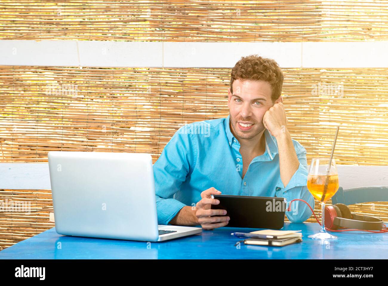 Junger Geschäftsmann, der im Urlaub mit Laptop und Tablet arbeitet. Fernbedienung. Neue Trends Tech-Konzept Stockfoto