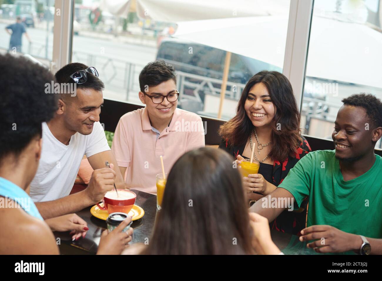 Multirassische glückliche junge Leute trinken Kaffee im Café, schwarz-weiße fröhliche Kumpels lachen Drinks genießen Spaß beim gemeinsamen Sitzen am Restauranttisch, verschiedene Freunde teilen sich das Mittagessen beim Treffen. Stockfoto