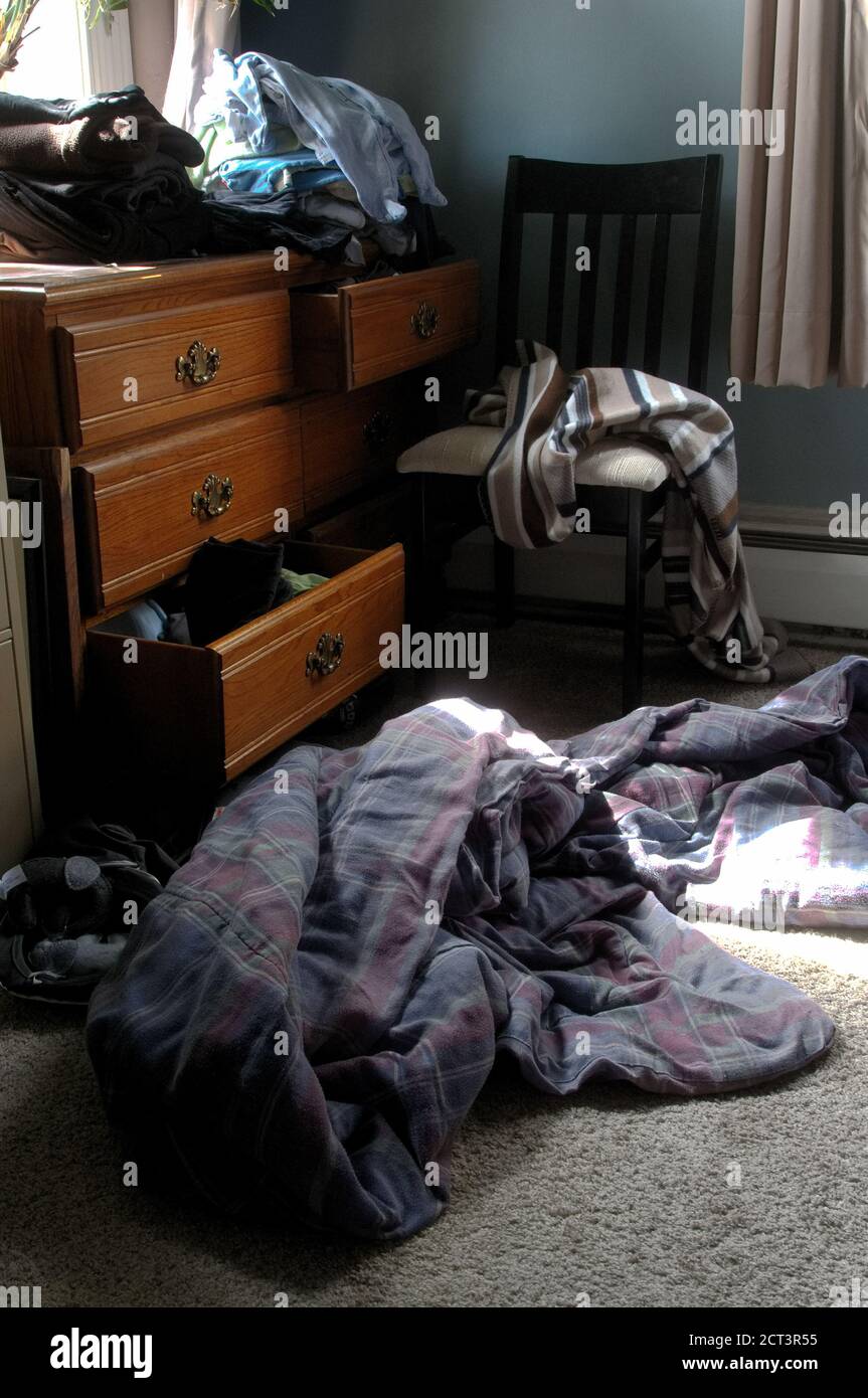 Offene Schubladen einer Kommode, ausgeklappte Decke auf dem Boden, und Unordnung in der Ecke eines sonnendurchfluteten Schlafzimmer Stockfoto