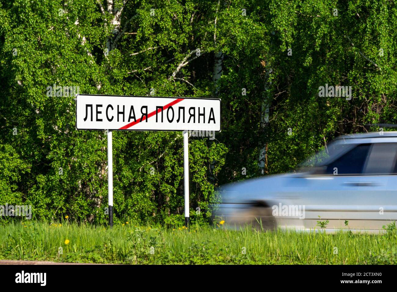 Straßenschild Ende der Stadt Lesnaya Polyana oder Lesnaya Polyana, Satellitenstadt Kemerowo, grüner Wald, Gras und graues Auto verschwommen durch den Verkehr Stockfoto