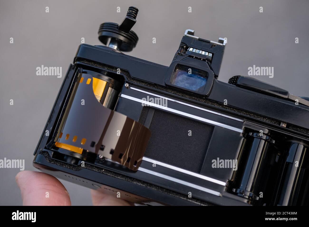 Eine Hand hält eine alte analoge Spiegelreflexkamera mit geöffneter Rückseite, wobei eine Rolle 35-mm-Farb-Negativfilm in die Spule gelegt wird, die geladen werden kann. Stockfoto
