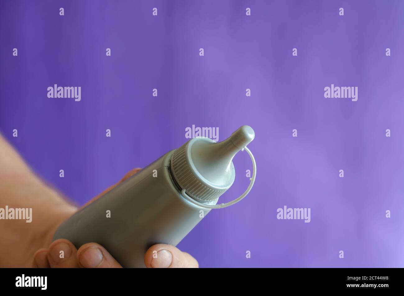 Männliche Hand und graue Plastikflasche mit Sirup. Der Mann hält eine neue Flasche Süßsirup für Eis und Desserts. Selektiver Fokus. Stockfoto