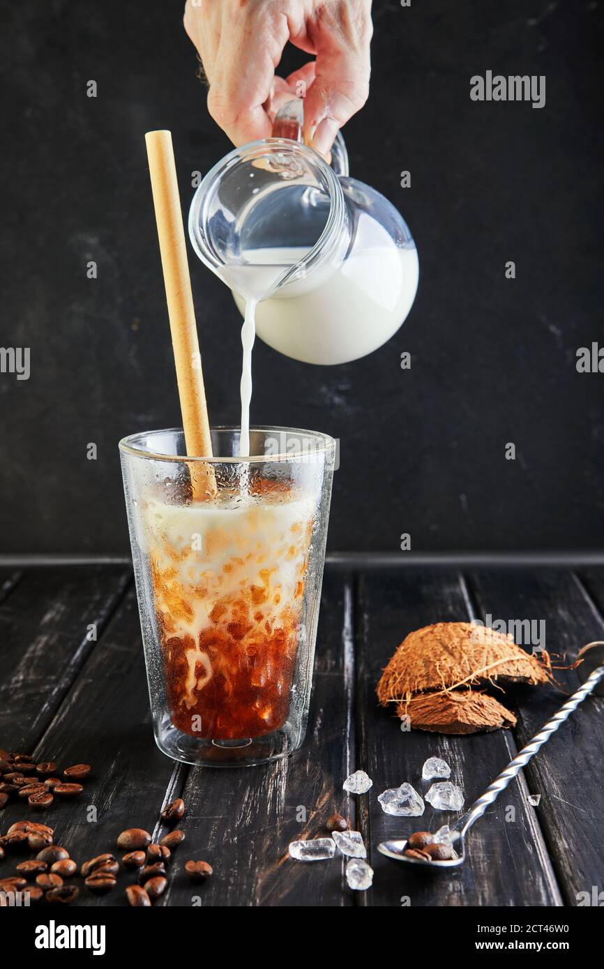 Eiskaffee im Thai-Stil mit Kokosmilch und Kaffeebohnen auf schwarzem Holzhintergrund. Stockfoto