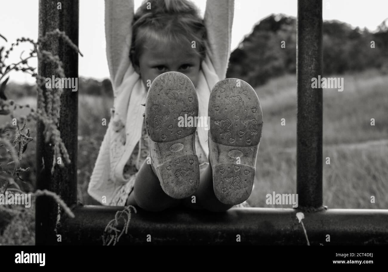 Nahaufnahme schwarz-weiß Foto von einem niedlichen kaukasischen Kind. Kindheitsmomente. Das Mädchen klettert und spielt draußen im Dorf die Eisenpfeife. Baby Stockfoto