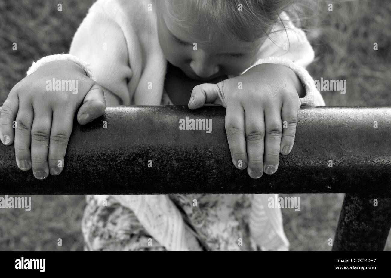 Nahaufnahme schwarz-weiß Foto von einem niedlichen kaukasischen Kind. Kindheitsmomente. Das Mädchen klettert und spielt draußen im Dorf die Eisenpfeife. Baby Stockfoto