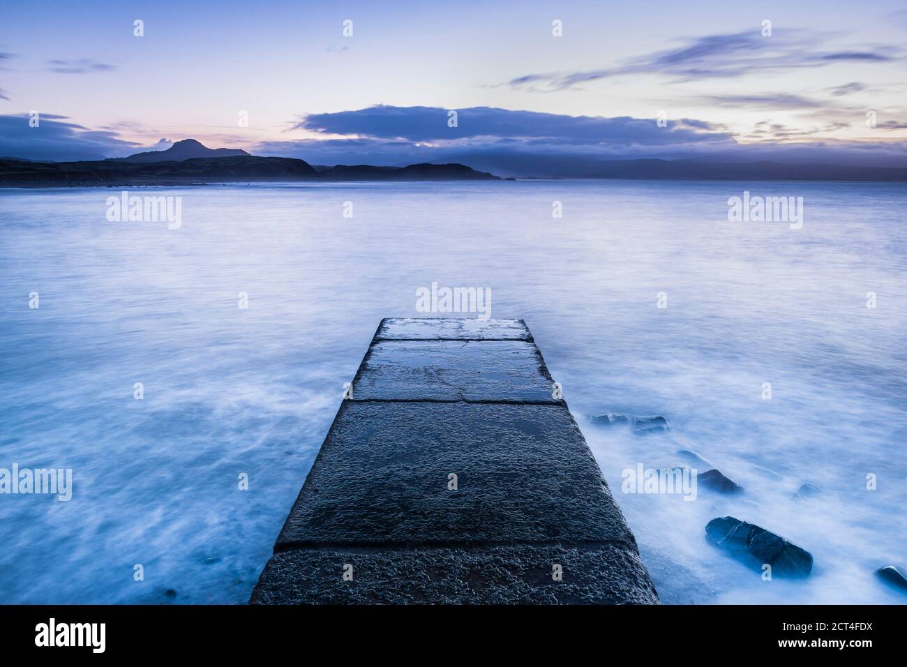 Langzeitbelichtung ruhige Szene der Wellen und des Ozeans mit einem Pier am Criccieth Beach bei Sonnenaufgang, Nordwales, Großbritannien Stockfoto