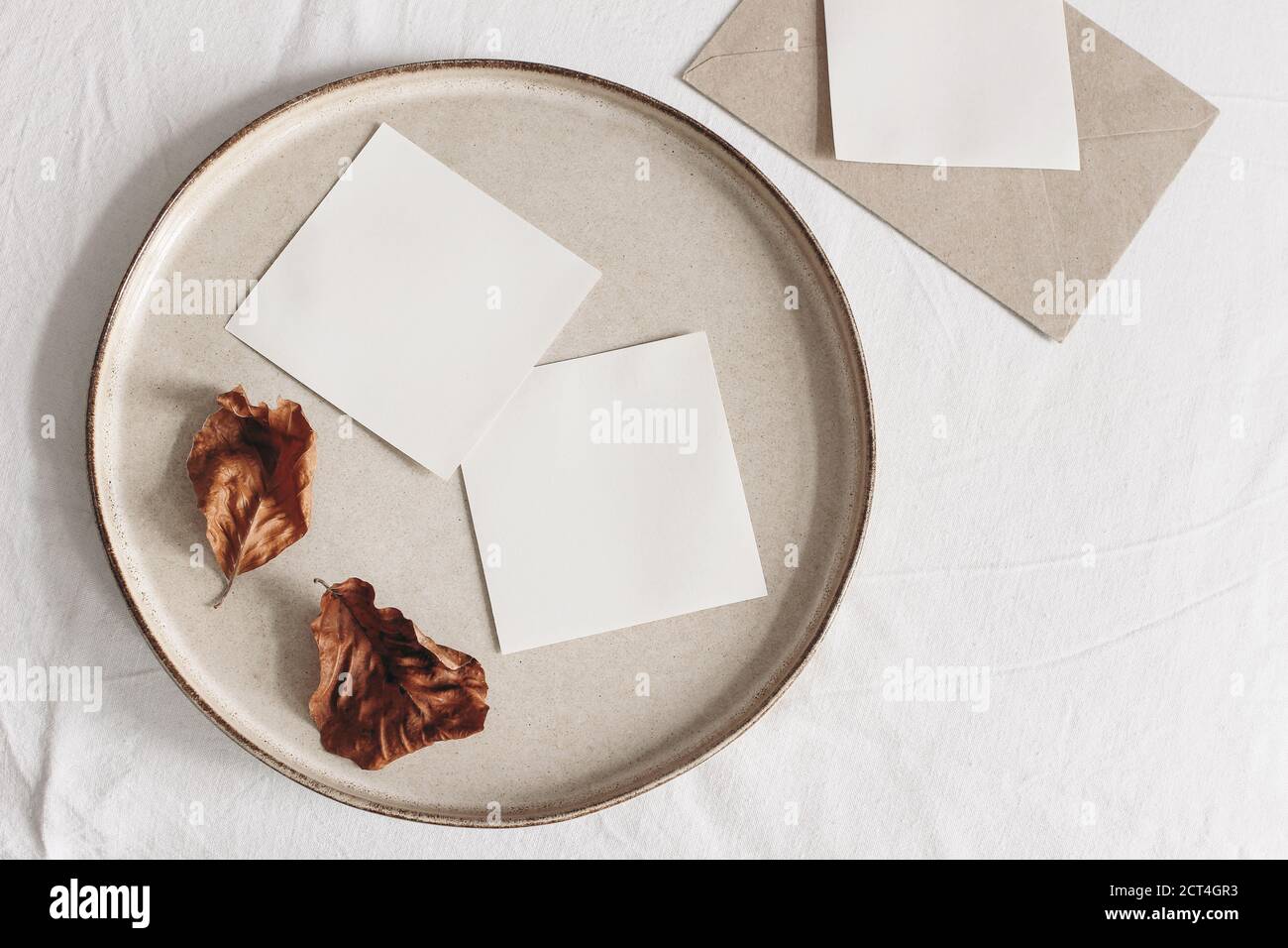 Herbstkomposition. Leere Memo-Karten Mockups, Bastelumschlag und trockene Buchenblätter auf weißem Leinentischtuch Hintergrund. Herbst und Thanksgiving Konzept Stockfoto